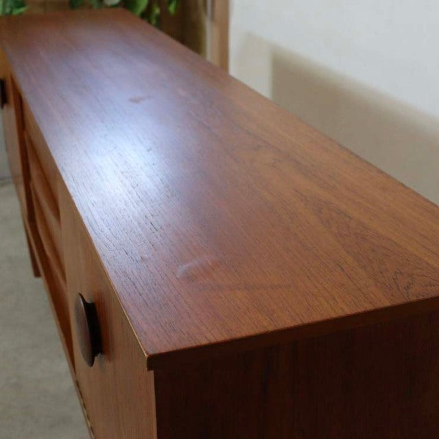 Mid-century vintage British teak sideboard with distinct wood grain, unique angled legs, and black handles.