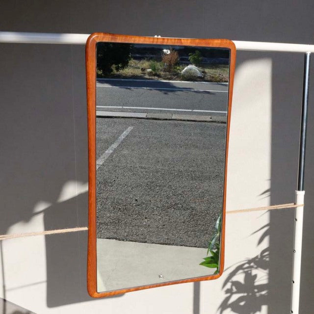 Vintage British mid-century teak wall mirror with rounded corners and smooth wood grain frame, rectangular shape, hanging on .