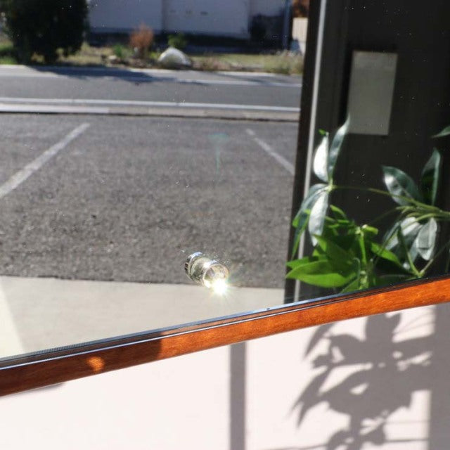 Mid-century British vintage teak wall mirror with rounded corners and smooth wood grain finish, reflecting outdoor scene and .