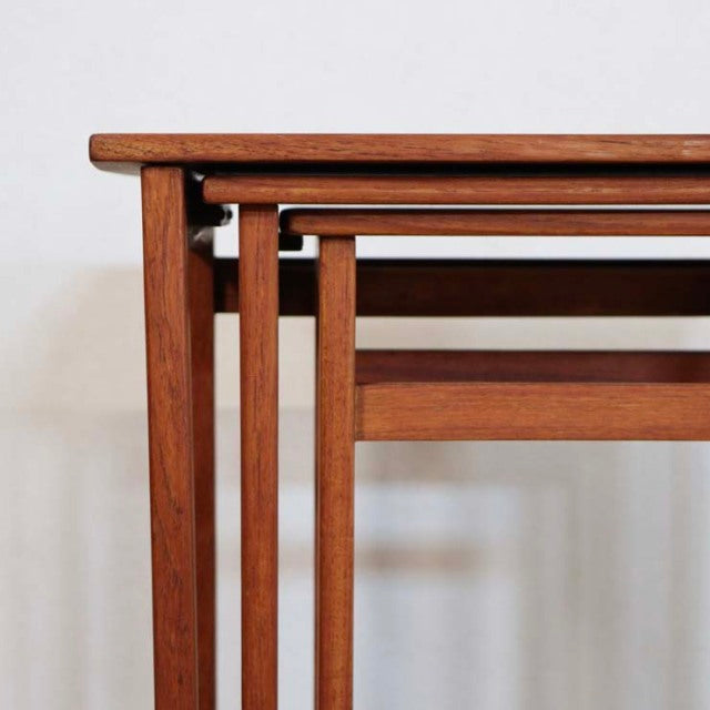 Set of vintage teak British mid-century nest tables with smooth wood grain and slender square legs nested together.