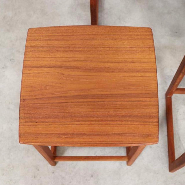 Vintage teak nesting tables with smooth wood grain and slender mid-century British legs on concrete floor.