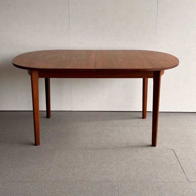 Oval mid-century vintage teak dining table with slender tapered legs, British-Denmark design, smooth wood grain surface.