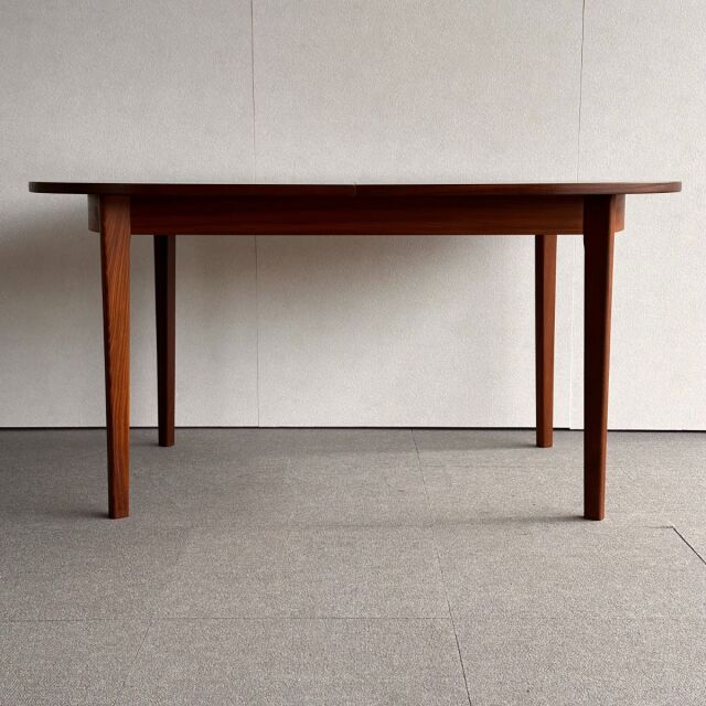 Mid-century British vintage oval dining table in rich teak with smooth wood grain and tapered legs.