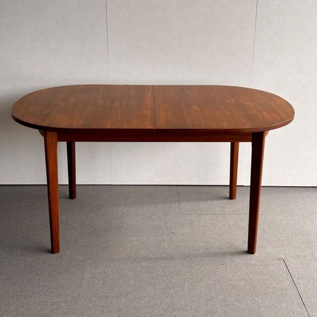 Oval vintage teak dining table with smooth wood grain, slender tapered legs, mid-century British-Denmark design.