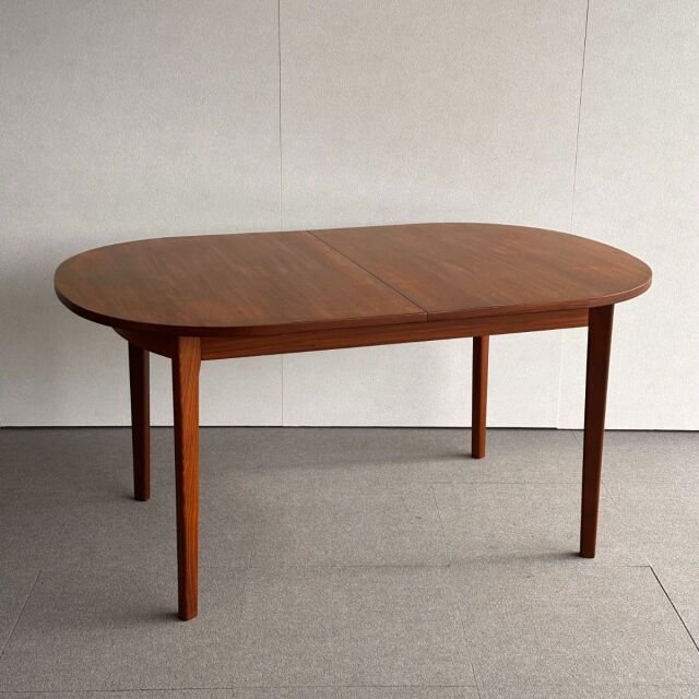 Mid-century British vintage teak dining table with oval top, smooth wood grain, and tapered legs.