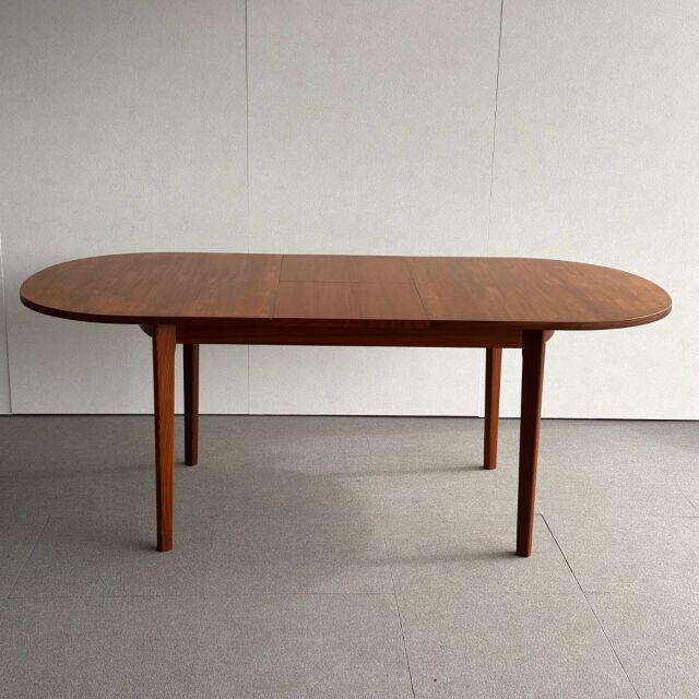 Vintage mid-century teak dining table with oval top, smooth wood grain, and slender British-style legs from Denmark.
