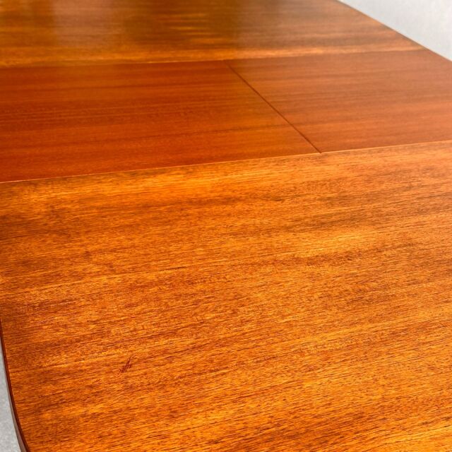 Vintage British mid-century teak oval dining table with smooth wood grain and tapered legs.