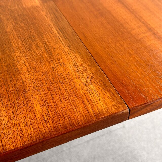 Close-up of vintage British mid-century teak dining table surface showing rich wood grain and smooth oval edges.