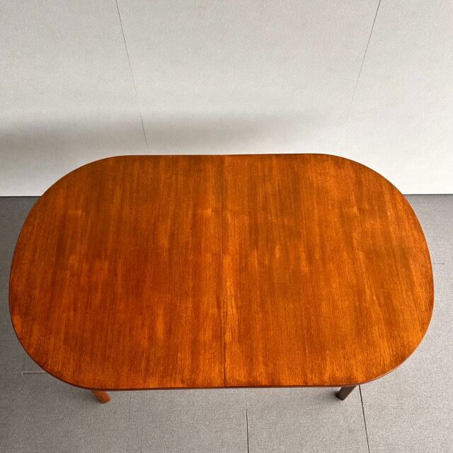 Mid-century British vintage teak dining table with smooth oval top and visible wood grain, slender rounded legs.