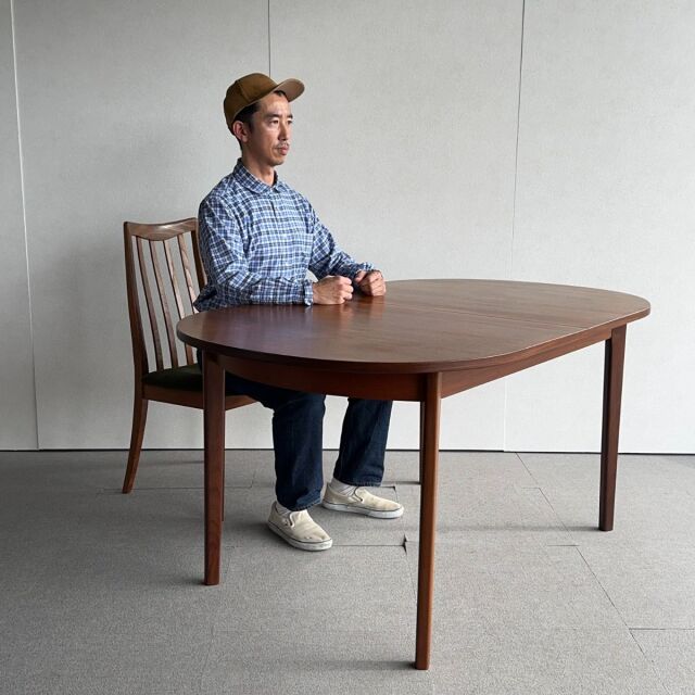 Vintage teak oval dining table with smooth wood grain, slender tapered legs, mid-century British and Danish design.