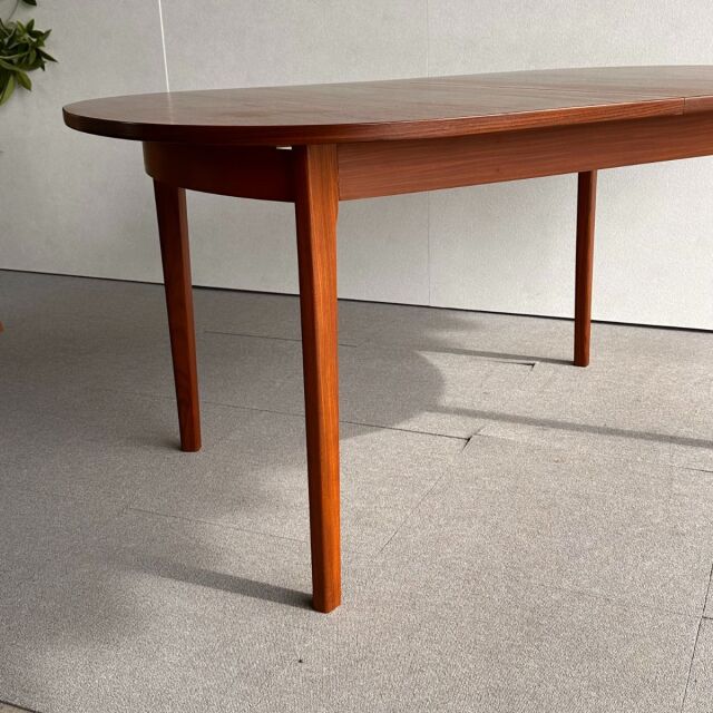 Mid-century British vintage oval dining table in teak with smooth wood grain and tapered legs.