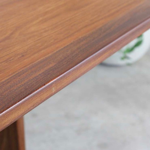 Close-up of vintage British G-Plan teak dining table corner showing rich wood grain and smooth rounded edge from mid-century .