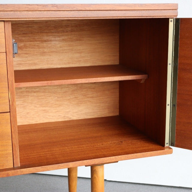 Vintage teak mid-century British sideboard by William Laurence, open cabinet showing wood grain, brass hinge, and rounded.