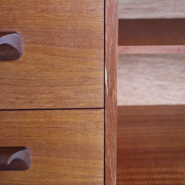 Close-up of vintage teak sideboard drawer front with smooth wood grain and distinctive carved wooden handles, mid-century.