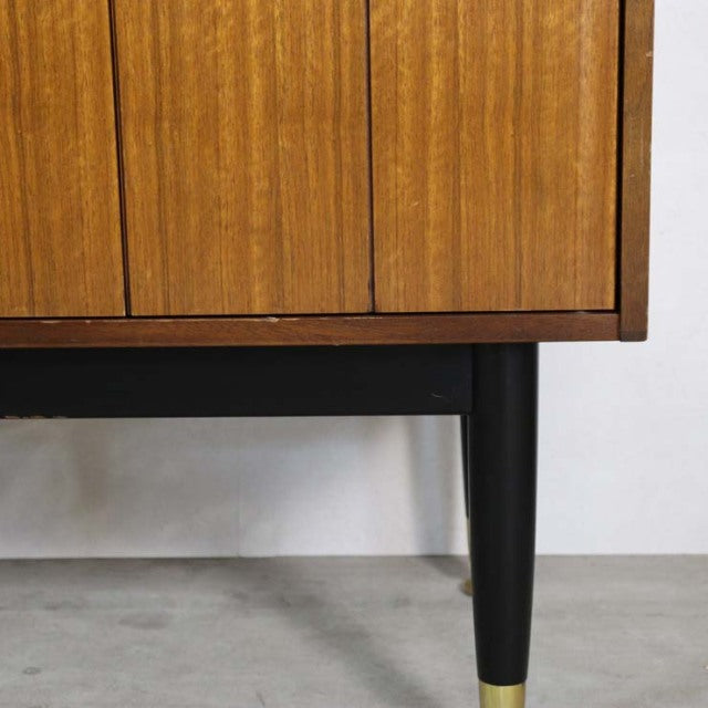 Close-up of vintage teak G-Plan Goldstamp sideboard corner showing mid-century British design, black tapered leg with brass.