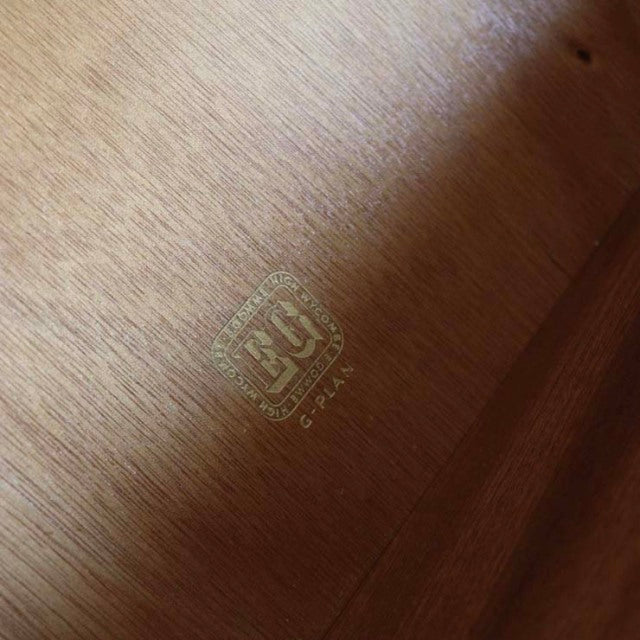 Close-up of vintage teak wood grain with gold G-PLAN GOLDSTAMP logo embossed, mid-century British craftsmanship from Denmark.