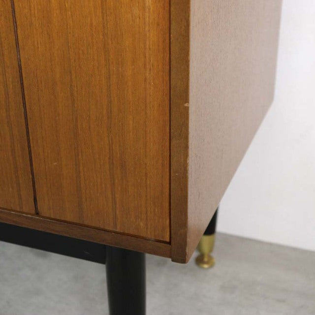 Vintage mid-century teak G-Plan Goldstamp sideboard corner showing wood grain and black tapered leg with brass foot.