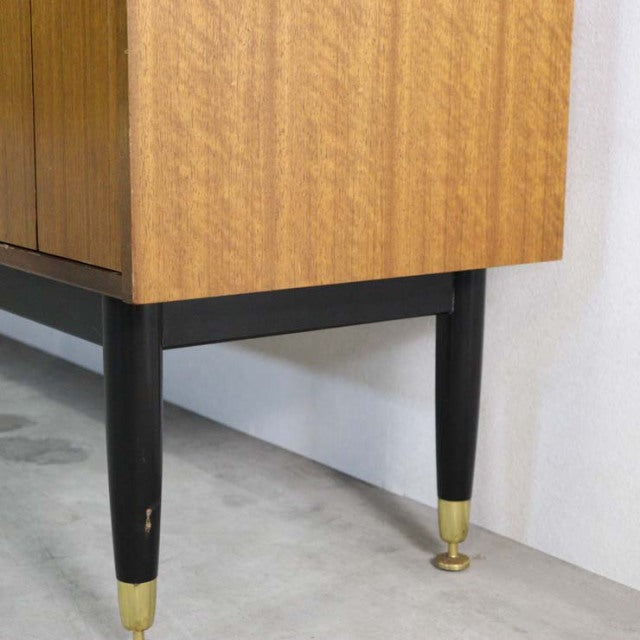 Mid-century British G-PLAN sideboard leg in black tapered wood with brass ferrule, teak veneer grain visible above.