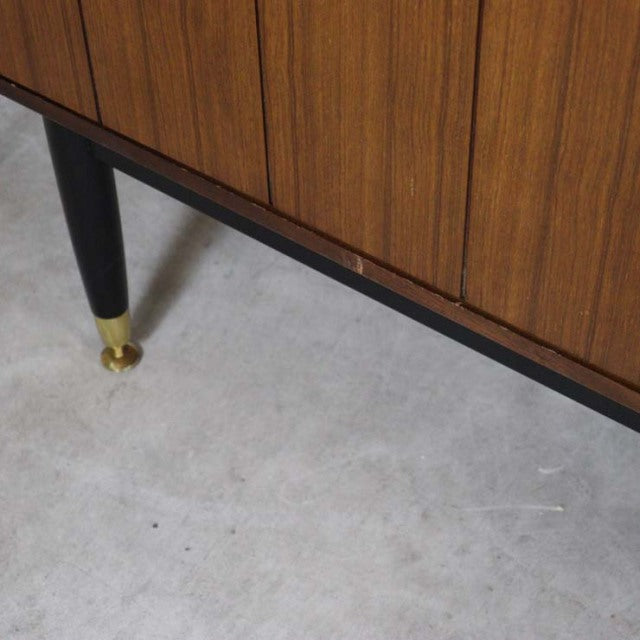 Mid-century British G-Plan teak sideboard with vertical wood grain, black tapered legs, and brass feet details.