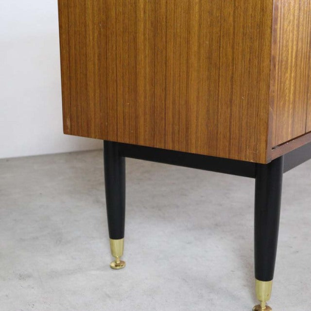 Mid-century British G-PLAN teak sideboard leg with black tapered wood and brass-capped foot on concrete floor.