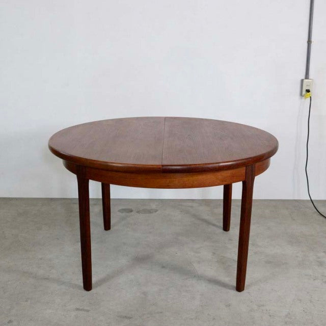 Round vintage teak dining table with mid-century British design, smooth wood grain and tapered legs.