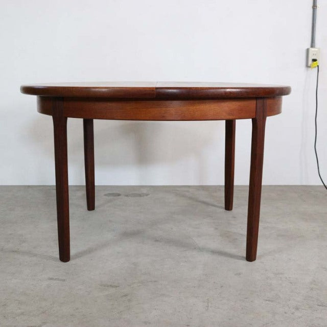 Round mid-century British vintage teak dining table by Elliotts of Newbury with smooth wood grain and tapered legs.
