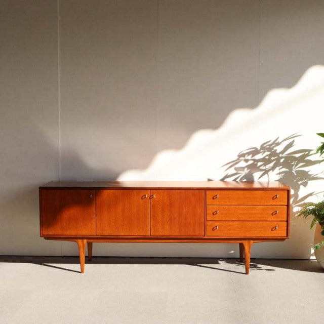 Vintage teak British mid-century sideboard by Younger with smooth wood grain, tapered legs, two-door cabinet, and four.