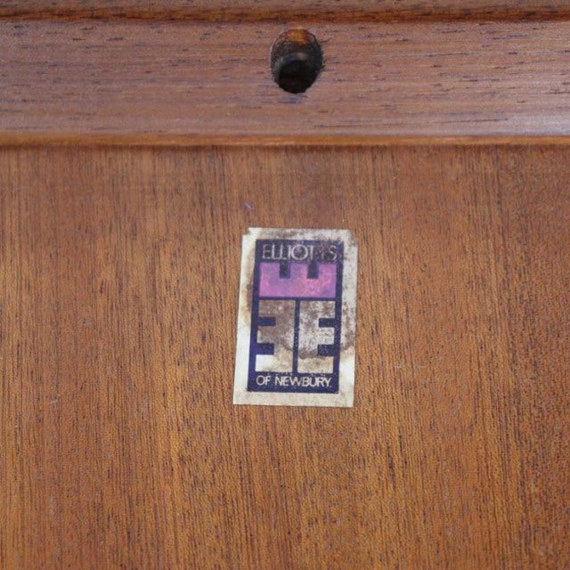 Close-up of a vintage British mid-century teak dining table showing rich wood grain and Elliotts of Newbury label on smooth.