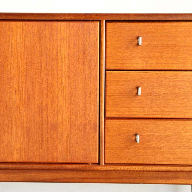 Vintage teak sideboard with smooth wood grain, British mid-century design, featuring three drawers with small rectangular.