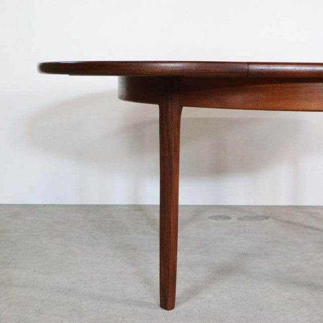 Mid-century British vintage dining table in teak with smooth wood grain and tapered round leg design.