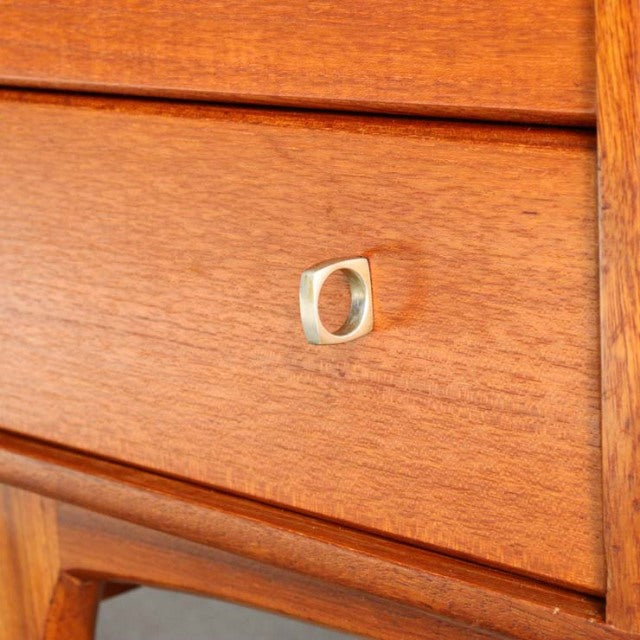 Mid-century British teak sideboard drawer with smooth wood grain and curved brass oval pull handle.