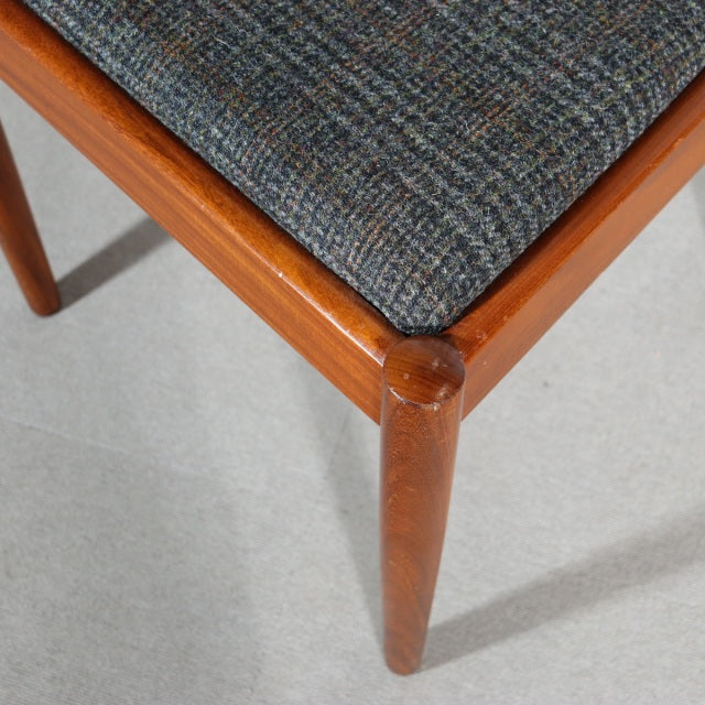 Close-up of vintage MEREDEW teak dining chair leg with smooth grain and textured dark gray upholstered seat, mid-century.