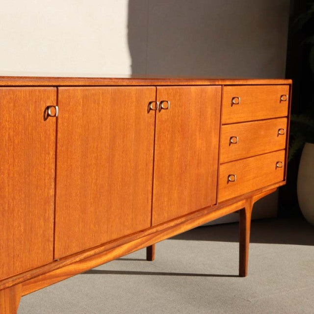 Mid-century British teak sideboard by Younger with rich wood grain, four drawers, and cupboard doors on slender tapered legs.