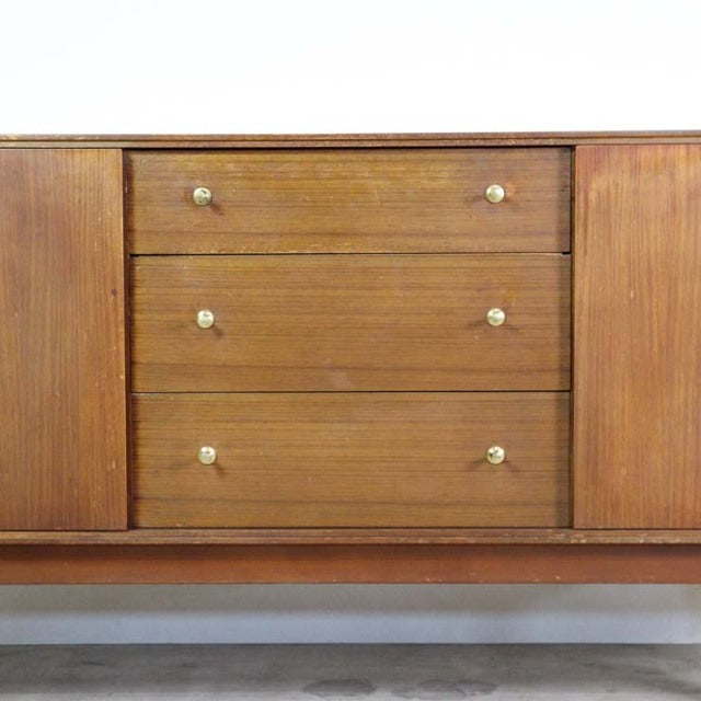 Vintage British mid-century teak sideboard with rich wood grain, three central drawers with round brass knobs, and sleek.