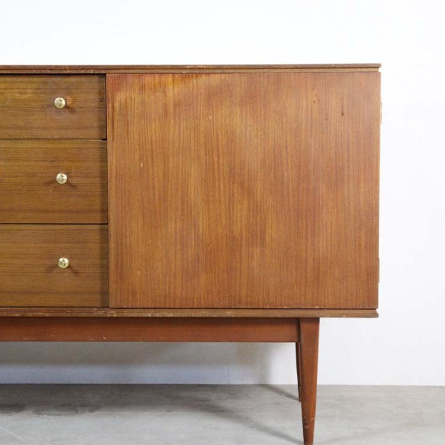 Mid-century British vintage teak sideboard with smooth wood grain, tapered legs, and brass drawer pulls.