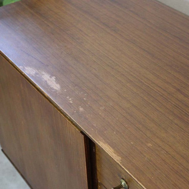 Vintage British mid-century teak sideboard with warm wood grain and brass drawer knobs, showing light surface wear on top.
