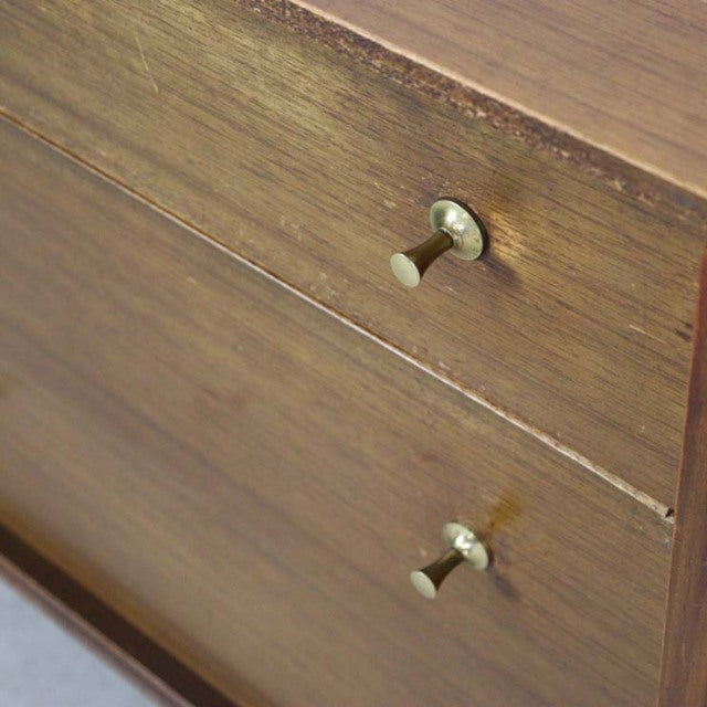 Mid-century British vintage teak sideboard drawer front with visible wood grain and brass knobs.