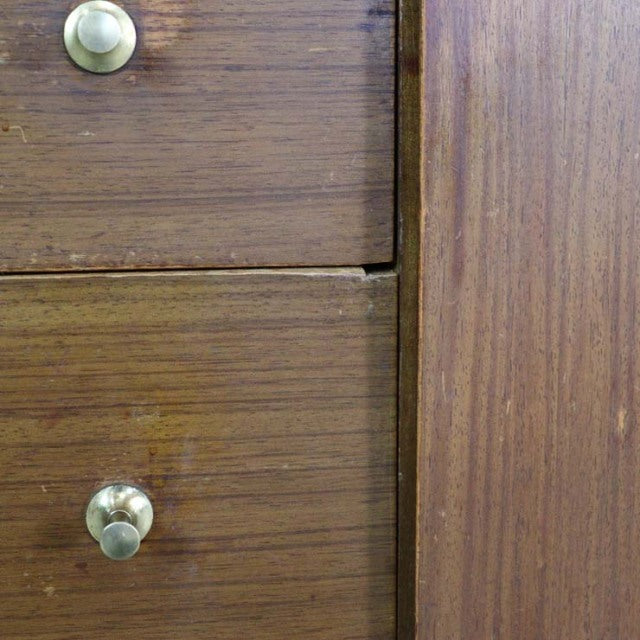 Close-up of vintage British mid-century teak sideboard drawer with brass knobs and visible wood grain.
