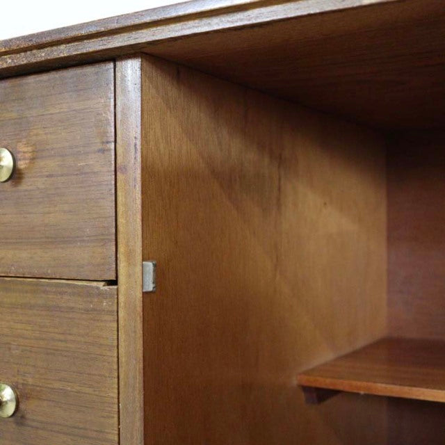 Close-up of vintage British mid-century teak sideboard showing drawer with brass knob, wood grain, and open shelf interior.