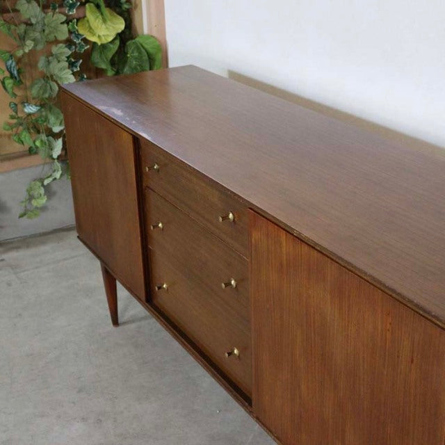 Vintage British mid-century teak sideboard with smooth wood grain, brass knobs, and tapered legs.