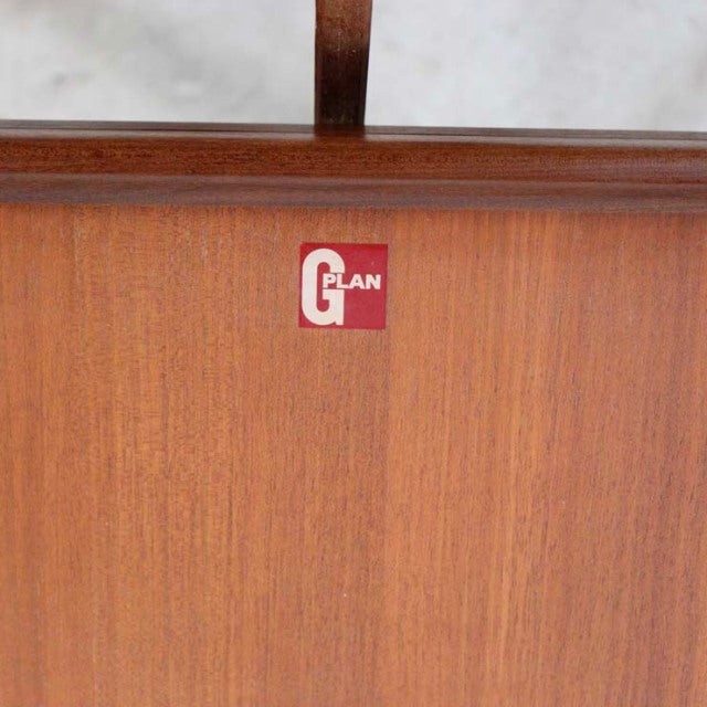 Close-up of vintage teak wood panel with G-Plan British mid-century furniture label, smooth grain visible.