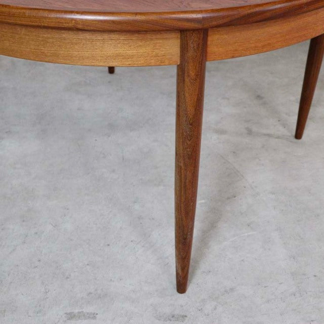 Mid-century British G-Plan vintage teak dining table leg with smooth wood grain and tapered cylindrical design on concrete.