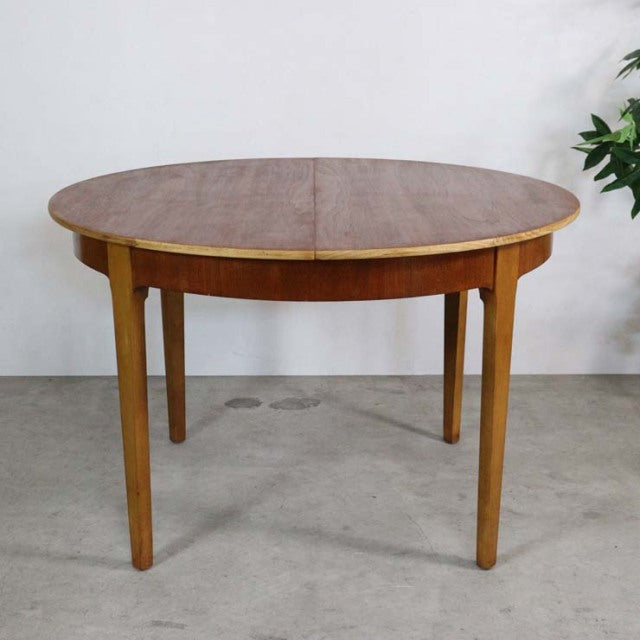 Round mid-century British vintage teak dining table with smooth wood grain and tapered legs.
