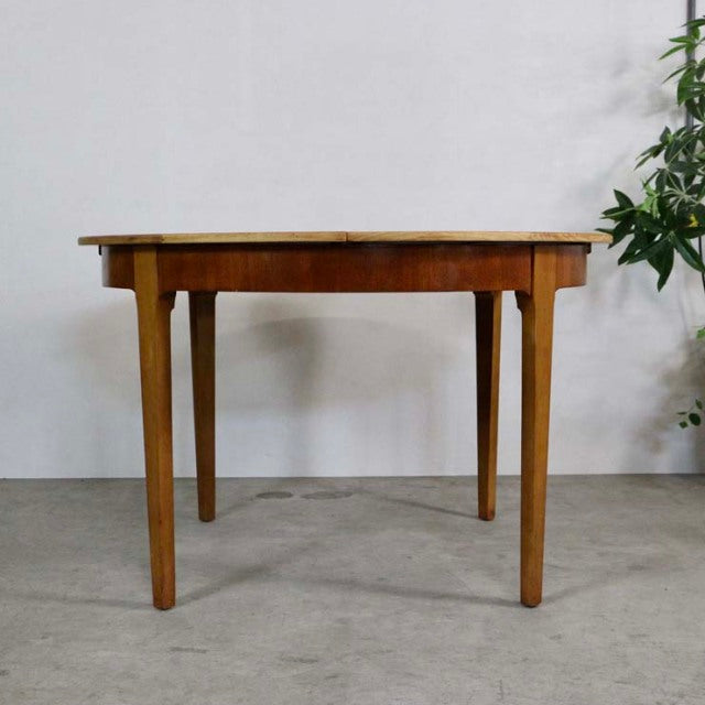 Round mid-century British vintage teak dining table with tapered legs and smooth wood grain finish.