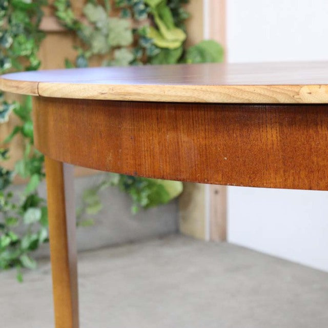 Vintage teak round dining table with smooth wood grain, slender tapered legs, mid-century British and Denmark design.
