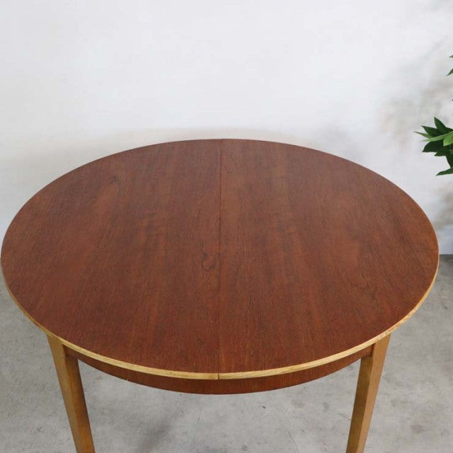 Round vintage teak dining table with smooth wood grain, slender tapered British mid-century legs, and warm Denmark-inspired.