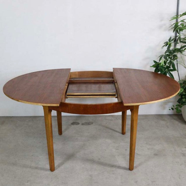 Mid-century British vintage teak round dining table with extending leaf, tapered legs, and visible wood grain.