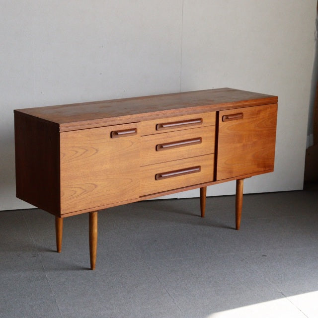 Vintage mid-century teak sideboard by William Laurence with smooth wood grain, tapered legs, and three drawers beside a.