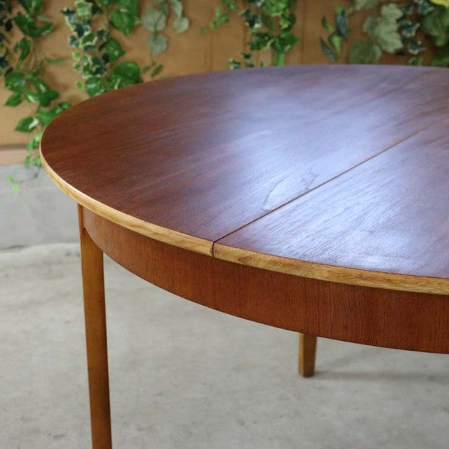 Mid-century British vintage teak round dining table with smooth wood grain and slender legs.