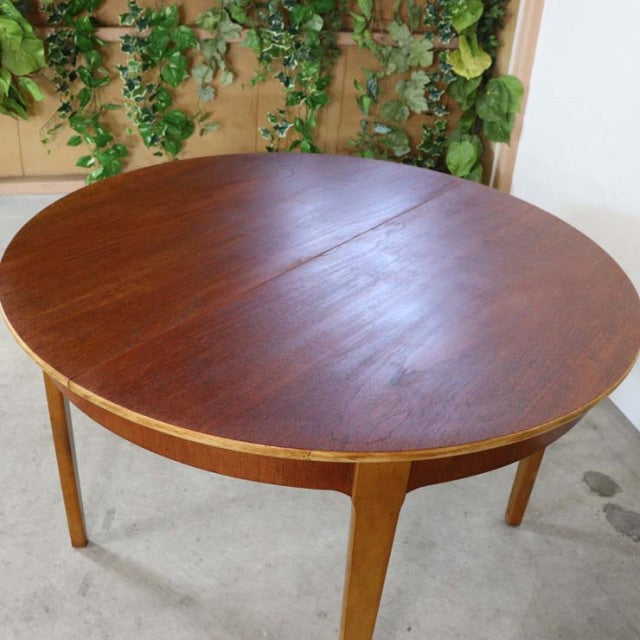 Round vintage teak dining table with mid-century British design, smooth wood grain surface, and slender tapered legs from.